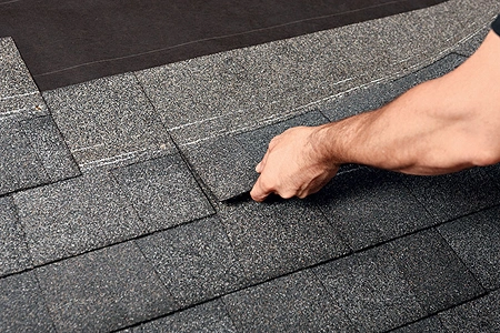 A roofing expert performing precise re roofing by layering new asphalt shingles over an existing roof.