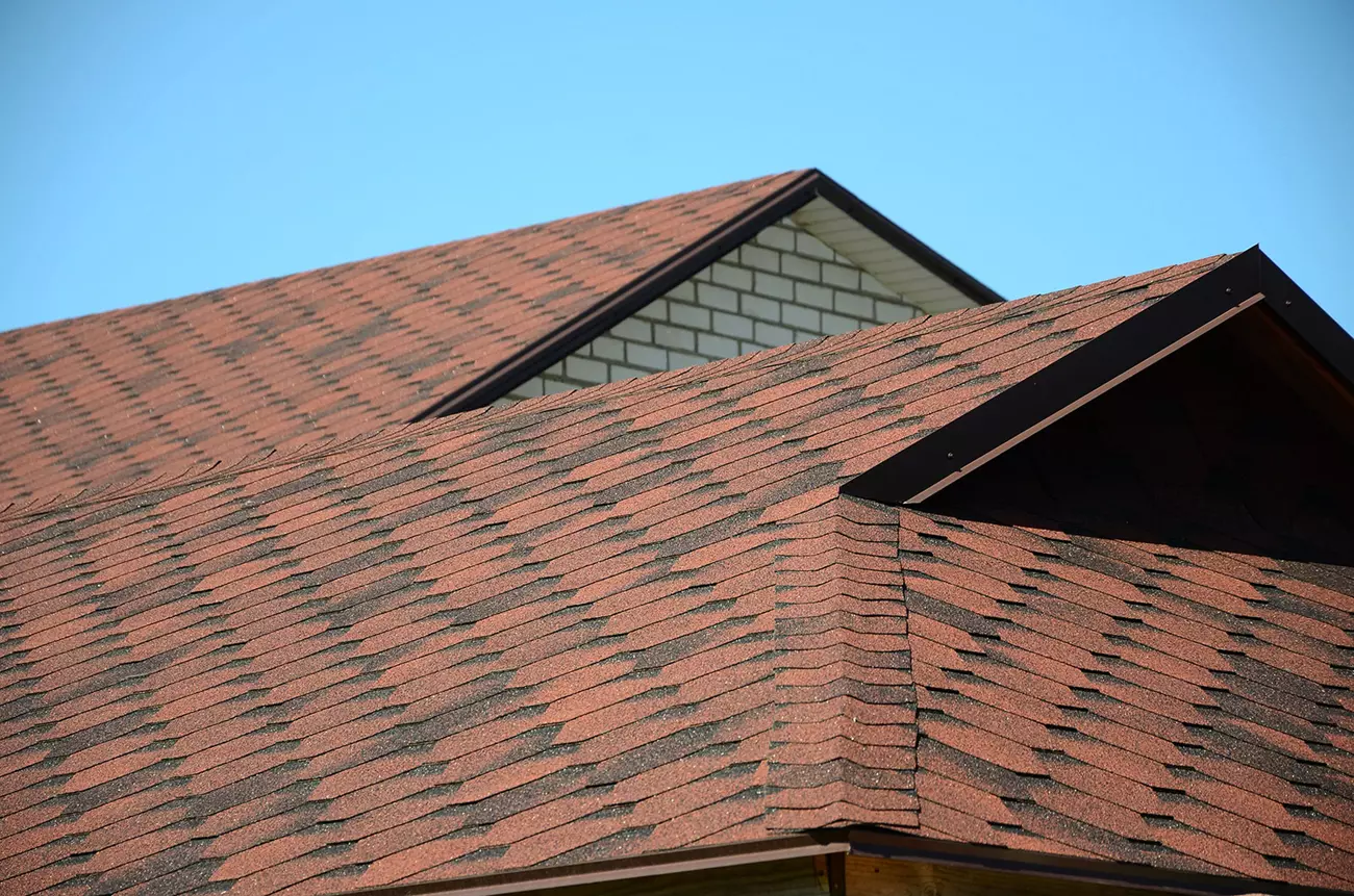 Completed asphalt shingle roof with multiple gables on a single-family home under a clear sky