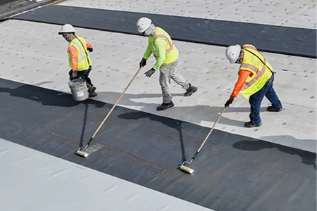 Three professional roofing contractors working together to install a high quality commercial flat roofing system.