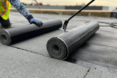 A roofing specialist rolling out modified bitumen for a high quality flat roof installation